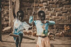 Two African children enjoy a playful moment on a swing outdoors.