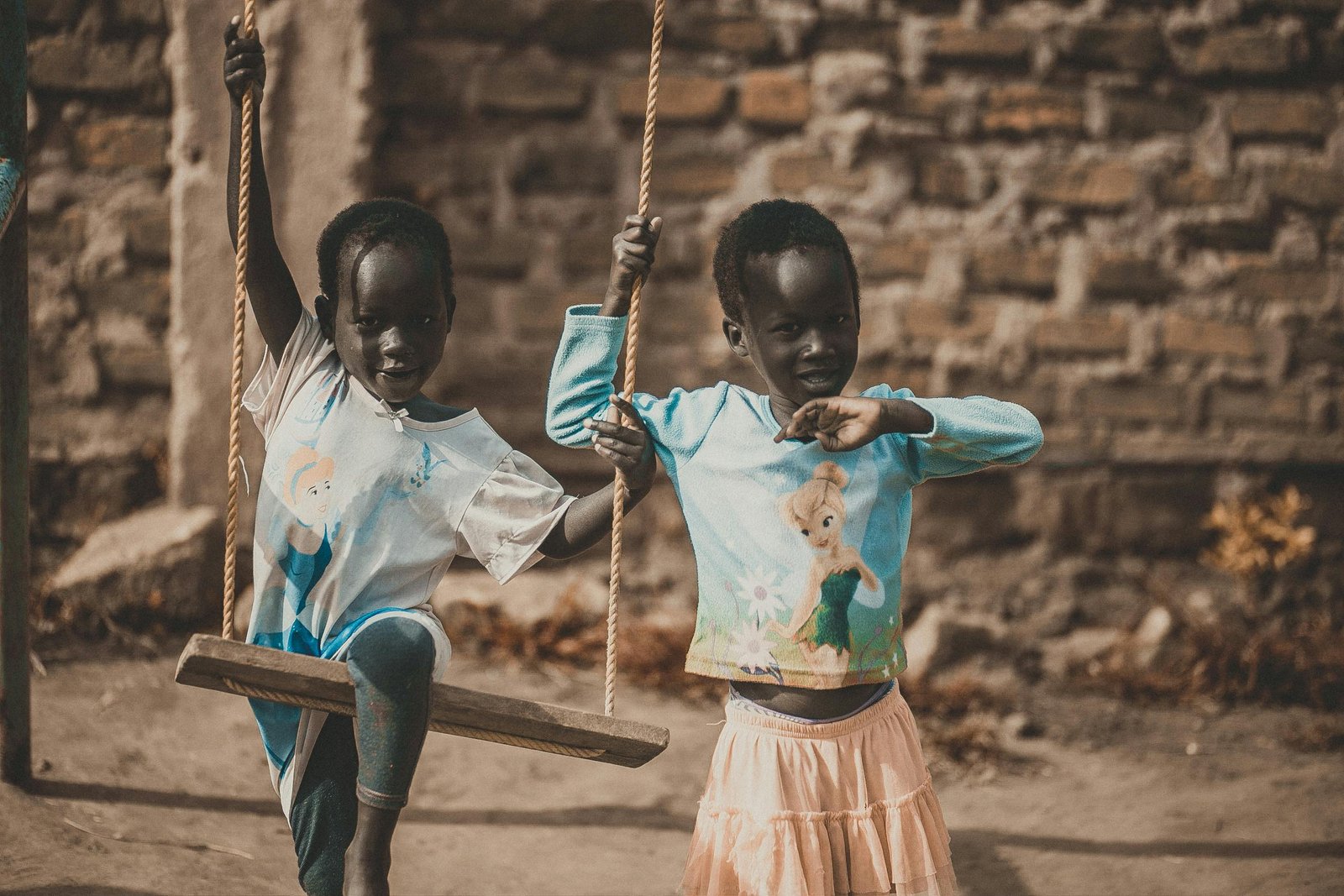 Two African children enjoy a playful moment on a swing outdoors.